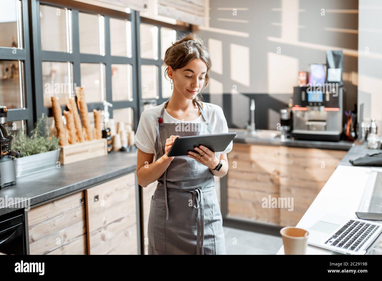 Junge Verkäuferin, die mit einem digitalen Tablet am Schalter eines Cafés oder Süßwarenladens arbeitet. Konzept eines kleinen Unternehmens und Technologien im Bereich Dienstleistungen Stockfoto