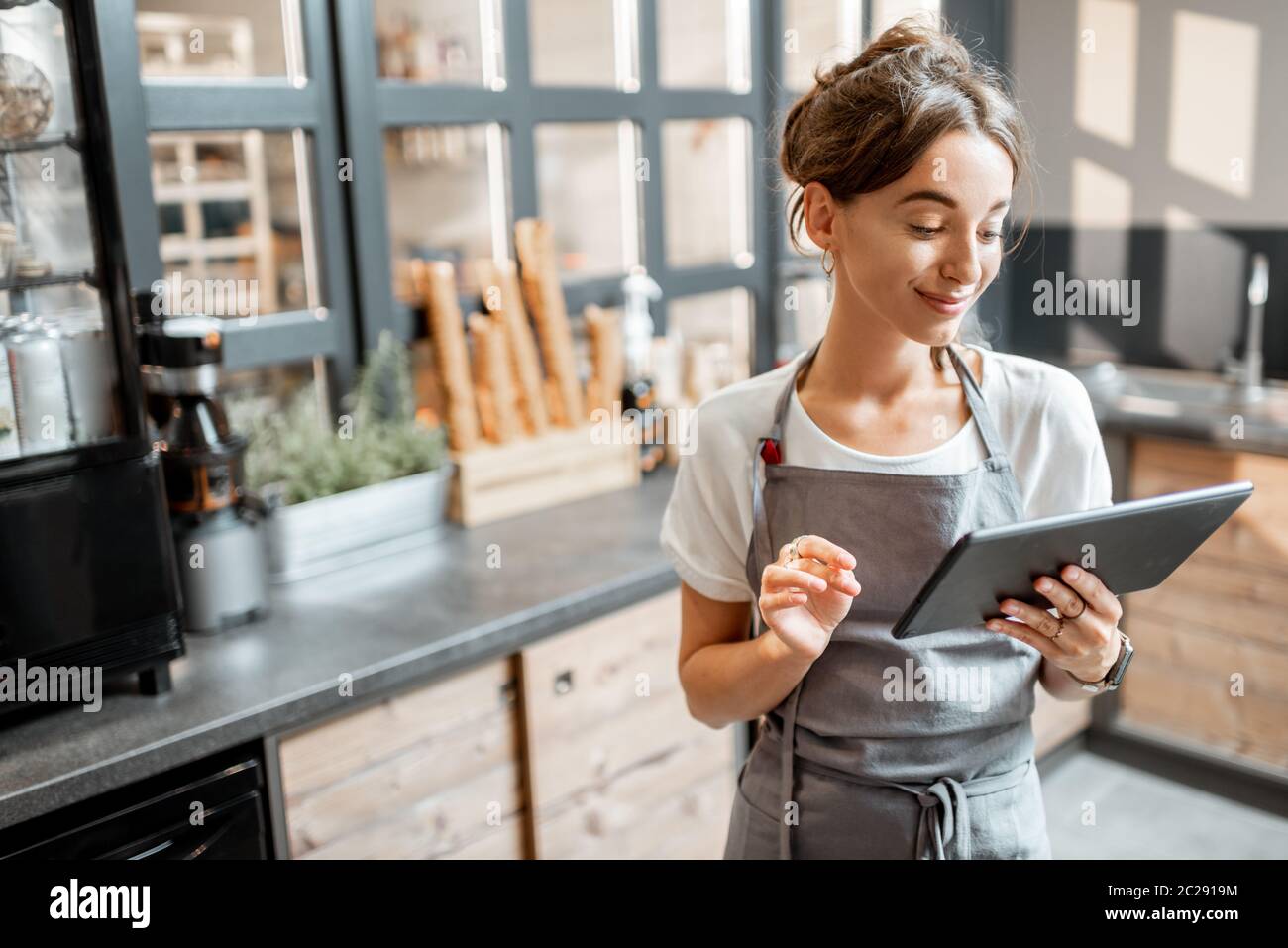 Junge Verkäuferin, die mit einem digitalen Tablet am Schalter eines Cafés oder Süßwarenladens arbeitet. Konzept eines kleinen Unternehmens und Technologien im Bereich Dienstleistungen Stockfoto