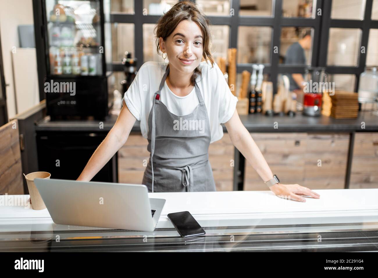 Porträt einer jungen Verkäuferin, die mit einem Laptop an der Theke in der Eisdiele oder im Café arbeitet. Konzept eines kleinen Unternehmens und des Einzelhandels Stockfoto