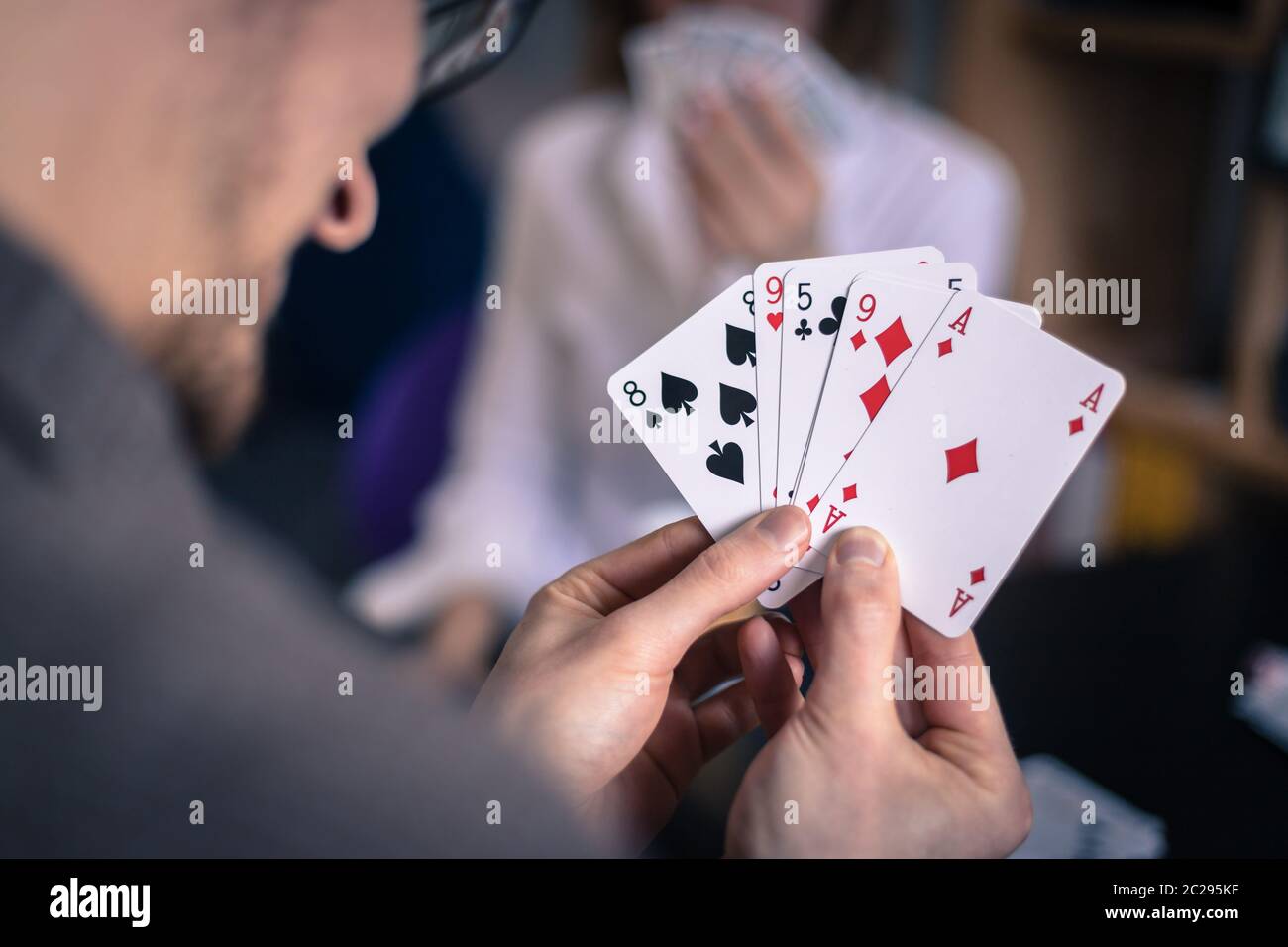 Freunde spielen zu Hause Karten zusammen. Der Mann hält Karten in den Händen, die Frau im verschwommenen Hintergrund. Stockfoto