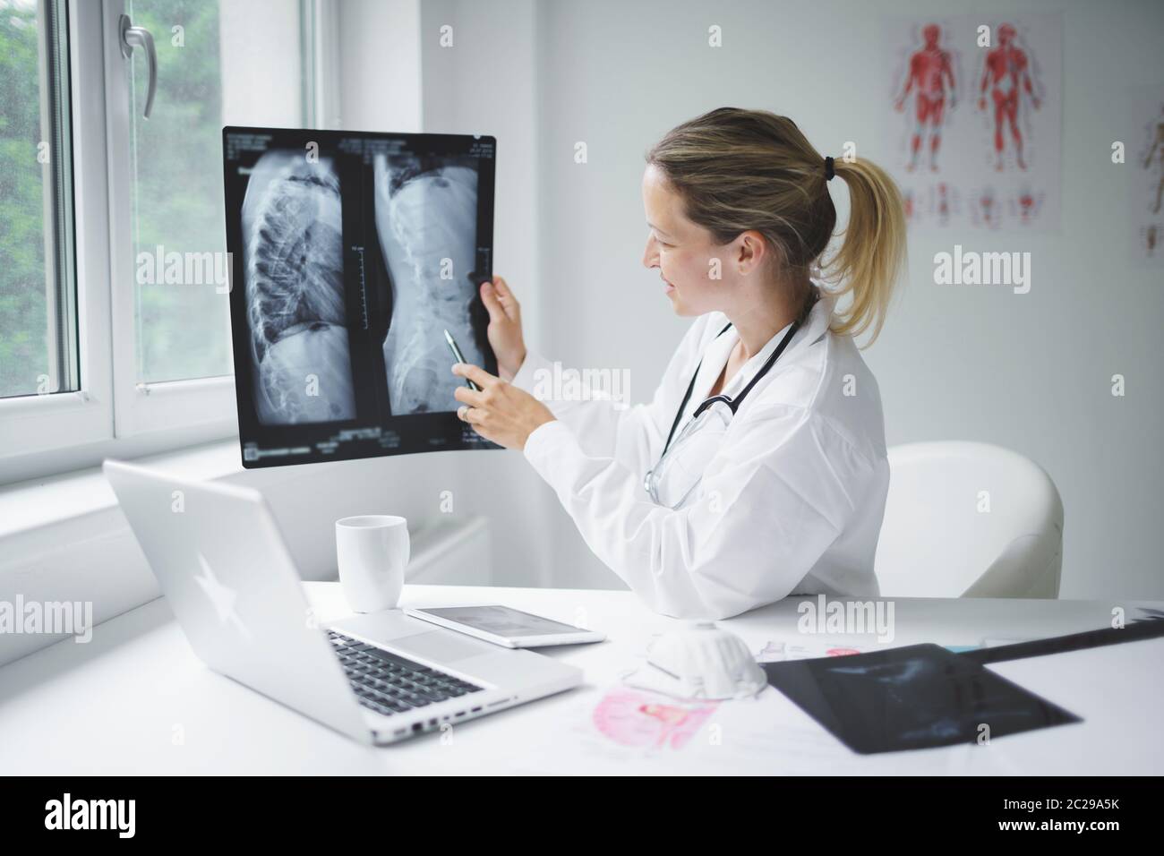 Hübsche und junge Ärztin diskutiert Röntgenbild online mit ihrem Patienten Stockfoto