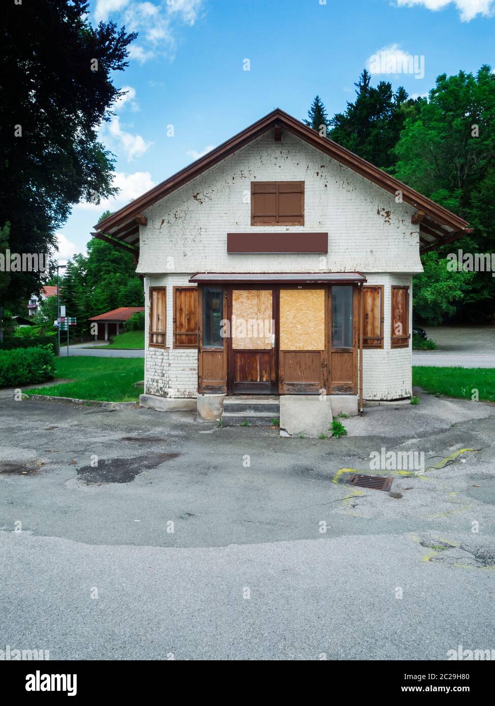 Frontale Gesamt-Ansicht eines mit Brettern und Holzplatten verschlossenen alten kleinen Bahnhofs-Kiosk in ländlicher bayerischer Umgebung mit Bäumen un Stockfoto