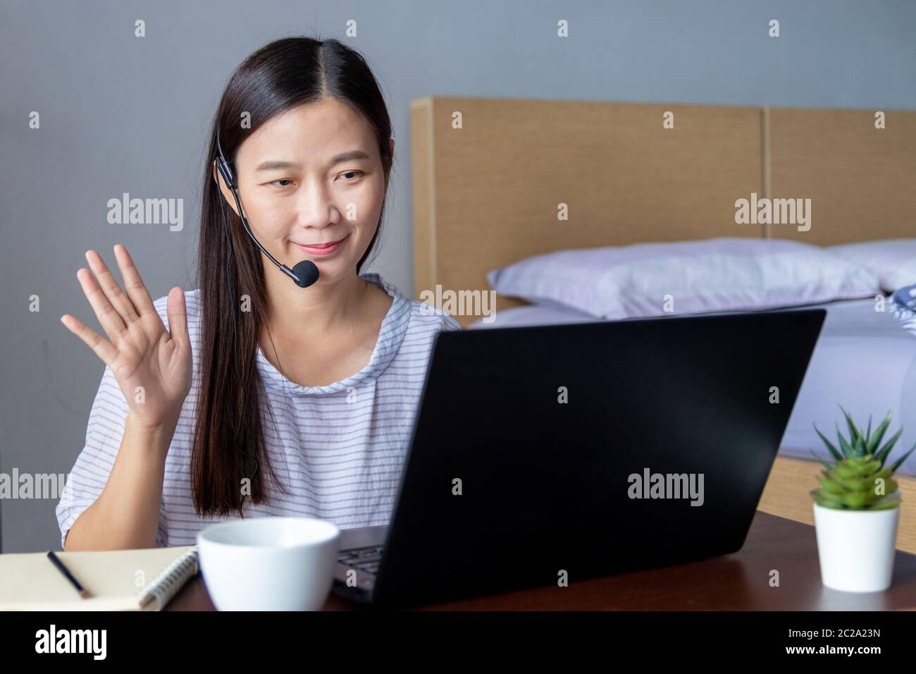 Arbeiten von zu Hause, neues normales Konzept. Attraktive glückliche Frau mit Headset macht Videokonferenzen mit Kollegen über Laptop-Computer. Stockfoto