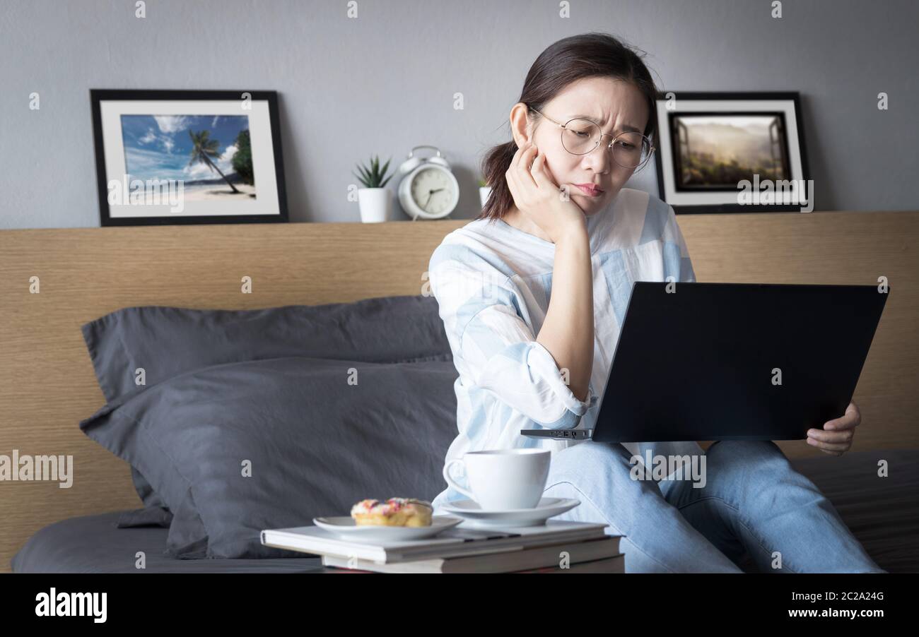 Arbeiten von zu Hause, neues normales Konzept. Frau arbeitet mit Laptop-Computer auf dem Bett aus ihrem Zimmer während der Selbstisolation mit Stress Emotion Stockfoto
