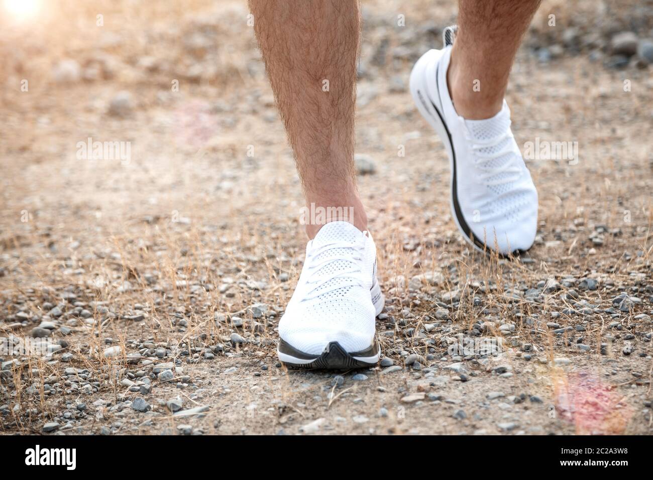 Die Füße der Männer in weißen Turnschuhen über unebenes Gelände laufen. Querfeldein laufen mit Fokus auf die Beine Runner. Stockfoto