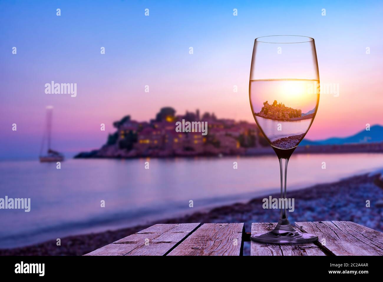 Weinglas auf alten hölzernen Tisch am Strand von Sveti Stefan bei Sonnenuntergang, Montenegro Stockfoto