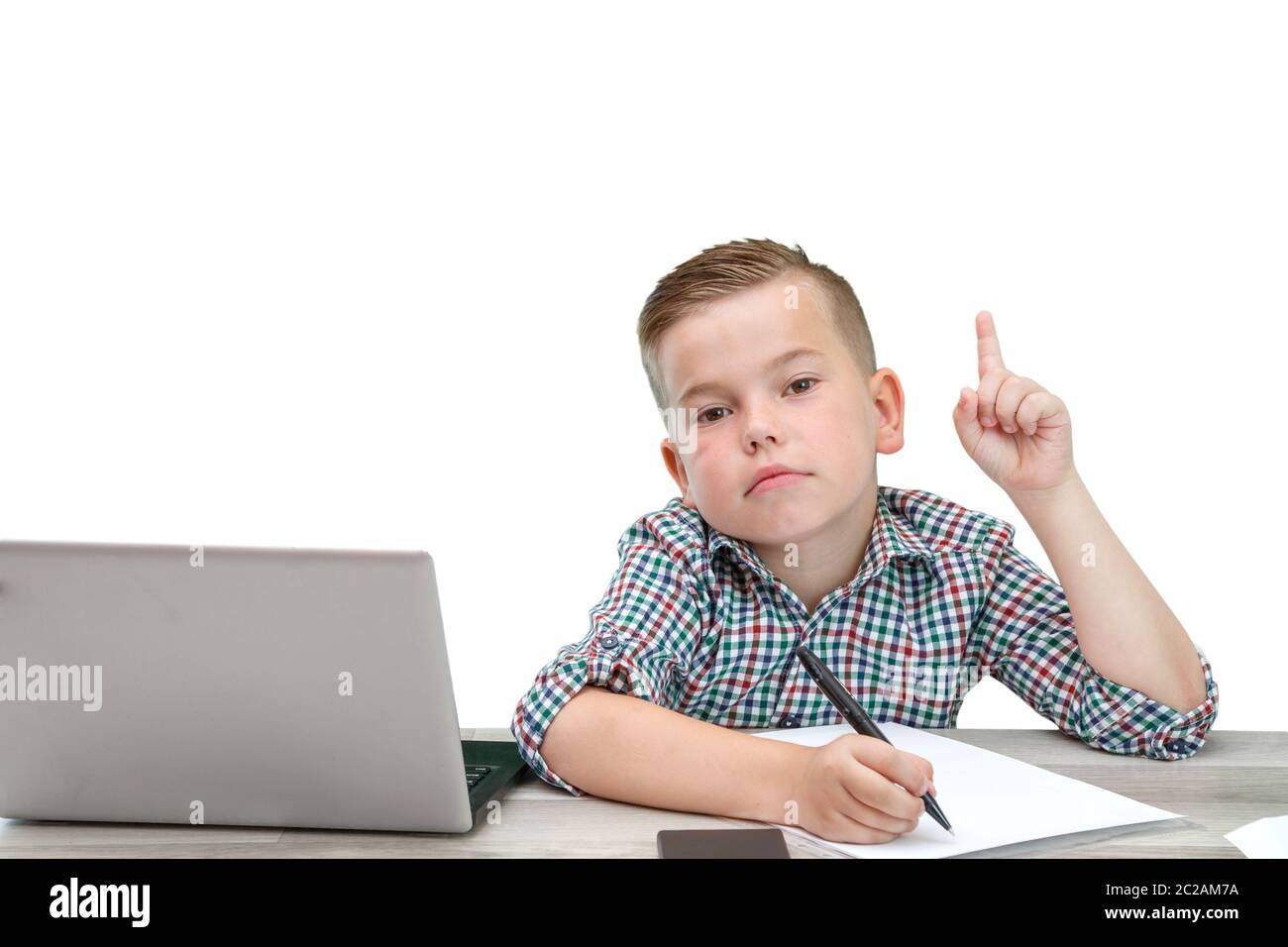 Kaukasischer Junge im Schulalter in einem karierten Hemd auf einem isolierten Hintergrund mit einem Laptop und einem Telefon zeichnet Gedanken in einem Stück Pap Stockfoto