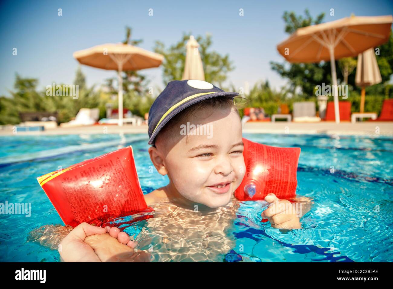 Ein kleiner Junge lernt in den Pool im Sommer zum Schwimmen mit der Unterstützung von den Händen seines Vaters Stockfoto
