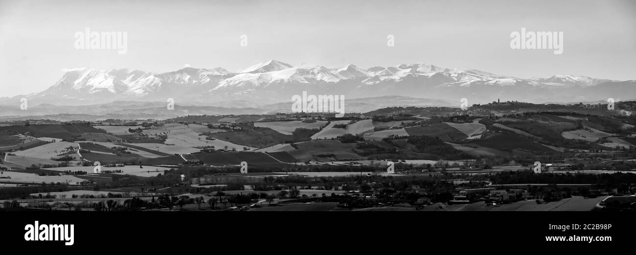 Panorama der gesamten Gebirgskette der Sibillini-Berge (Marken) von Recanati, teilweise schneebedeckt, in schwarz-weiß. Stockfoto