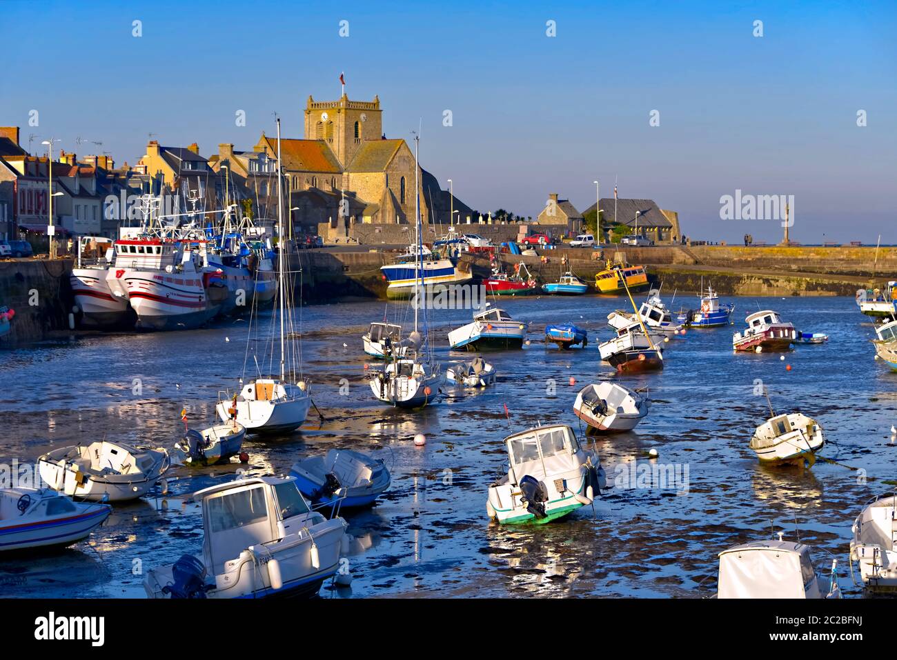 Hafen bei Ebbe am Ende des sonnigen Tages und Kirche Saint-Nicolas von Barfleur, eine Gemeinde auf der Halbinsel Cotentin in Frankreich Stockfoto