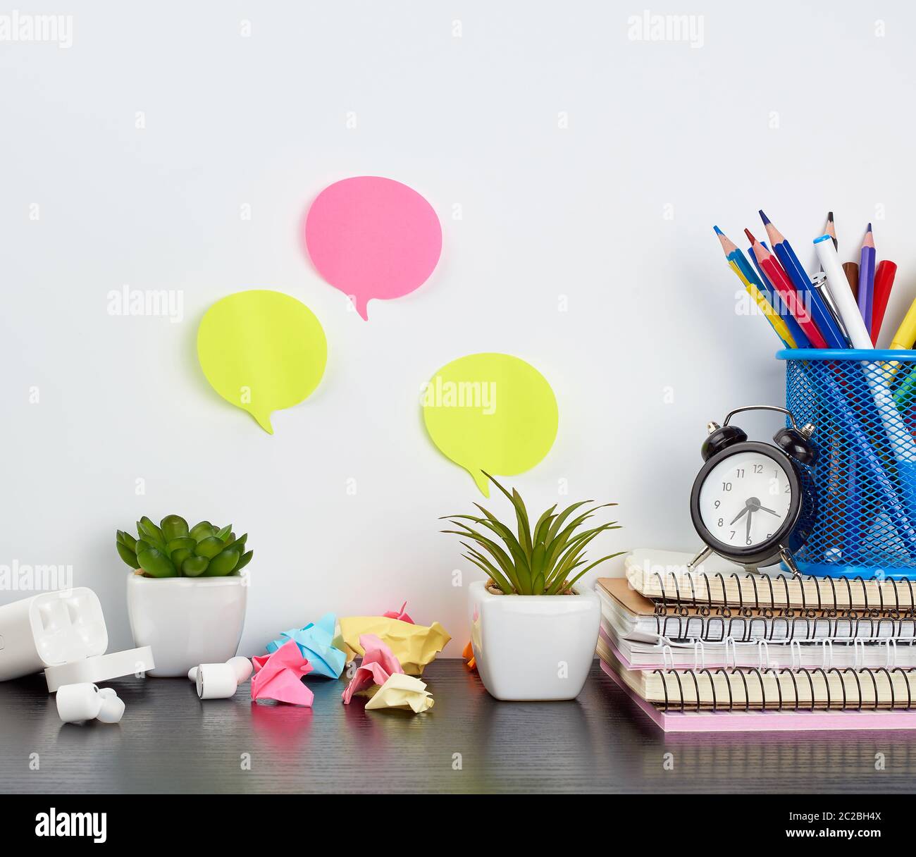 Stapel von Notebooks, Buntstifte in einem blauen Glas, grüne Pflanzen in Töpfen und kabellose Kopfhörer auf einem schwarzen Holztisch, Platz für ein Designer und fr Stockfoto