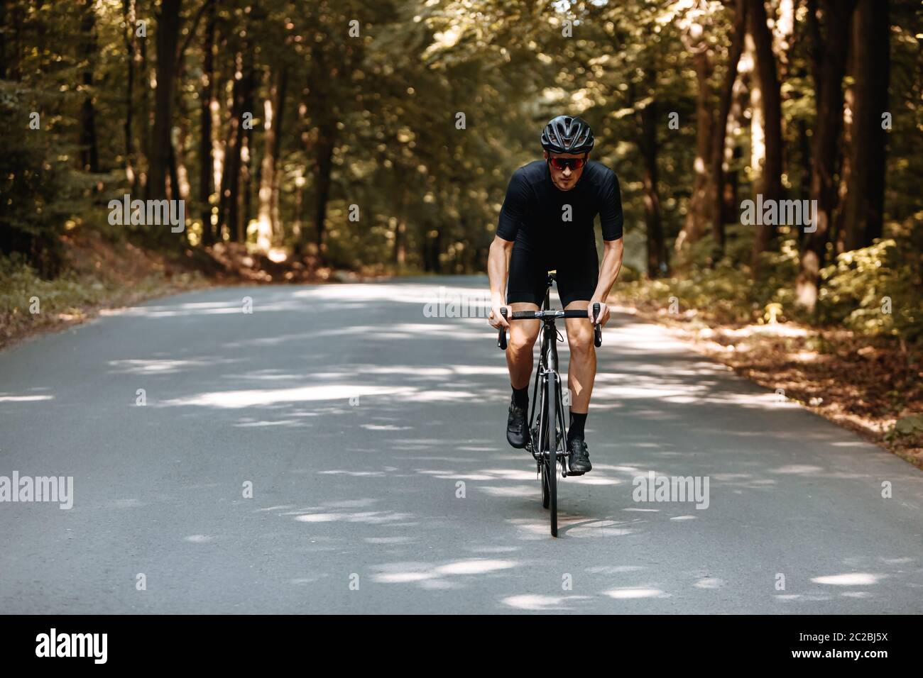 Starker männlicher Athlet in Radbekleidung, schwarzem Helm und Spiegelbrille, der an sonnigen Tagen Fahrrad fährt. Konzept der Selbstdisziplin und regelmäßige tra Stockfoto