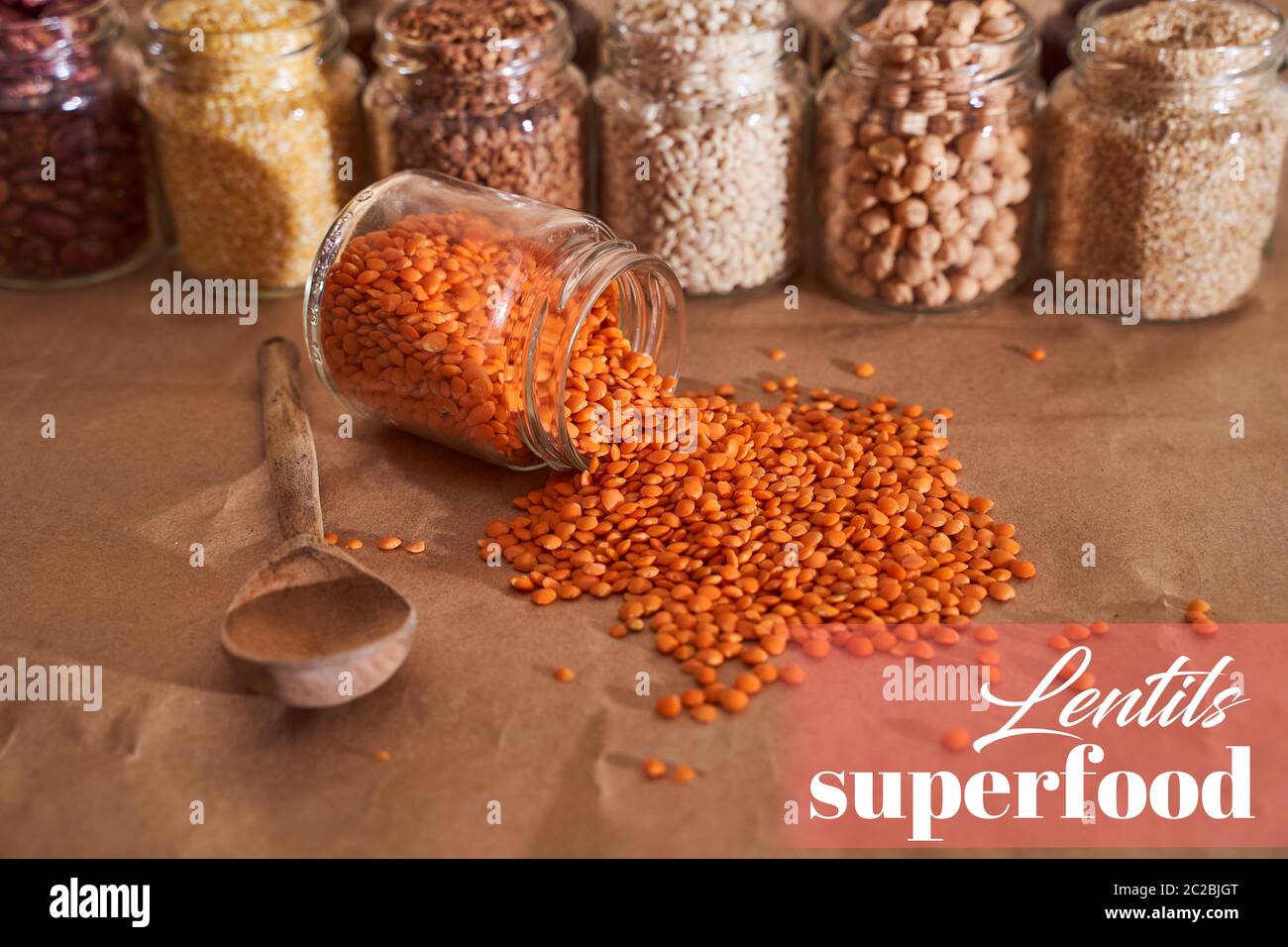 Rote Linsen mit Holzlöffel Nahaufnahme. Vor dem Hintergrund eines Kessens mit anderen Getreidearten. Superfood. Textdesign-Effekt Stockfoto