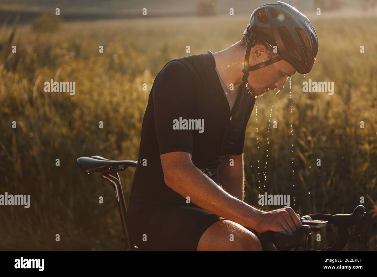 Seitenansicht eines reifen Radfahrers mit müdem nassen Gesicht, das schwarzen Helm trägt und Sportkleidung, die auf dem Fahrrad im Freien sitzt. Bärtiger Mann, der sich ausruhte Stockfoto