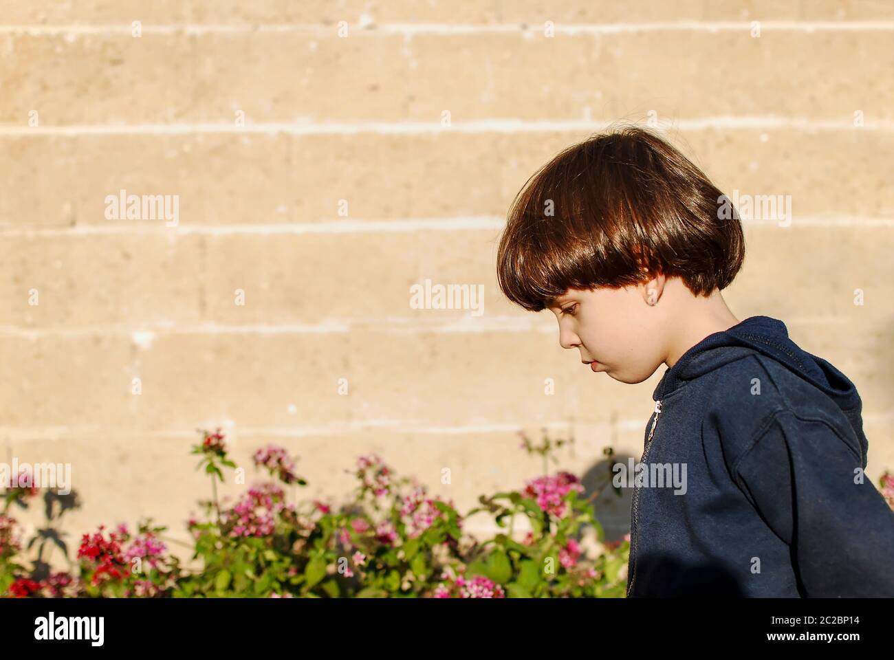 Kleiner trauriger Junge von sechs Spaziergängen mit dem Kopf, der tief in einem Garten gehalten wird Stockfoto