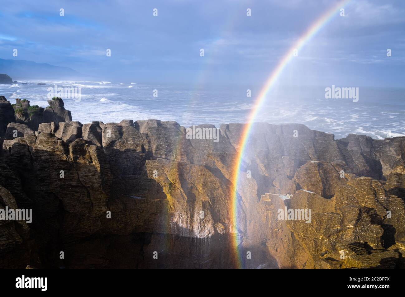 Ein doppelter Regenbogen wird durch Meeresspray in der Luft gebildet, nachdem bei Punakaiki an der Westküste der Südinsel Neuseelands ein großes Blowhole ausbricht. Stockfoto