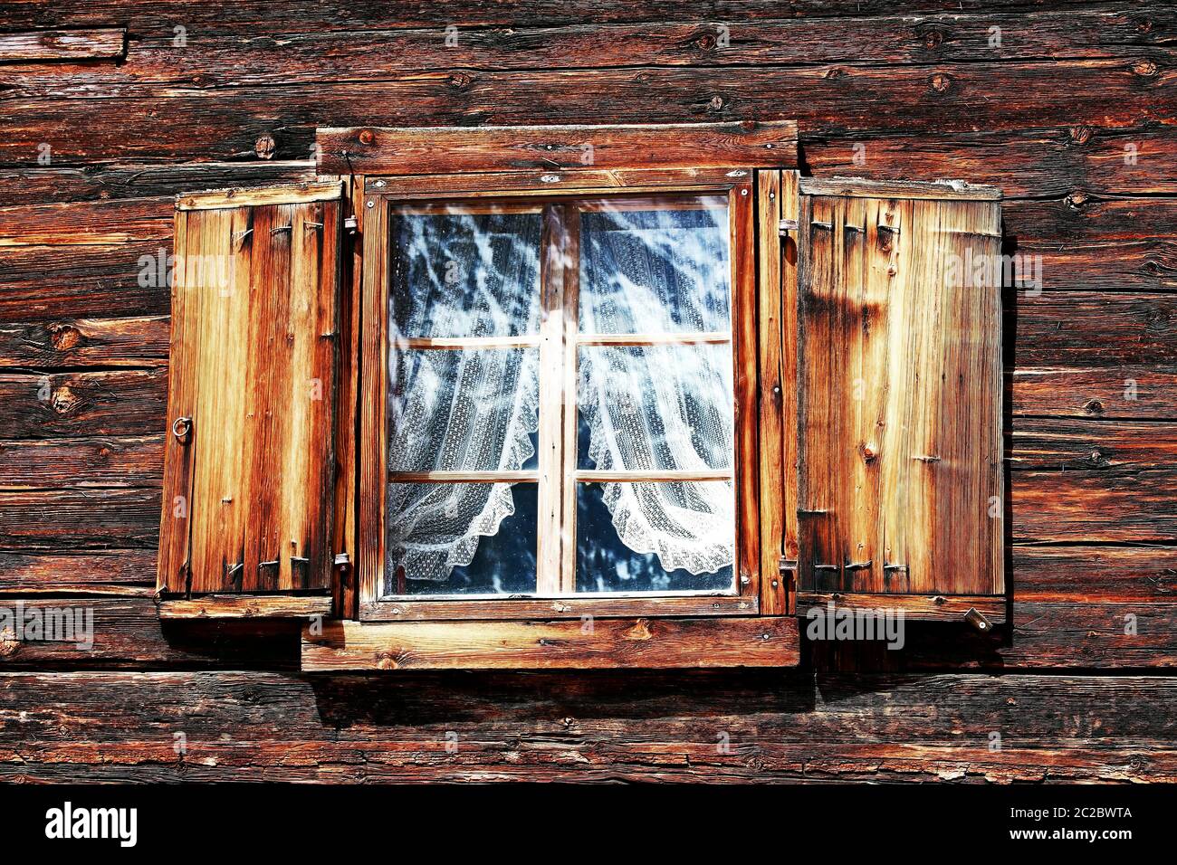 Fenster mit Vorhängen und Fensterläden auf einem alten Holzhaus Stockfoto