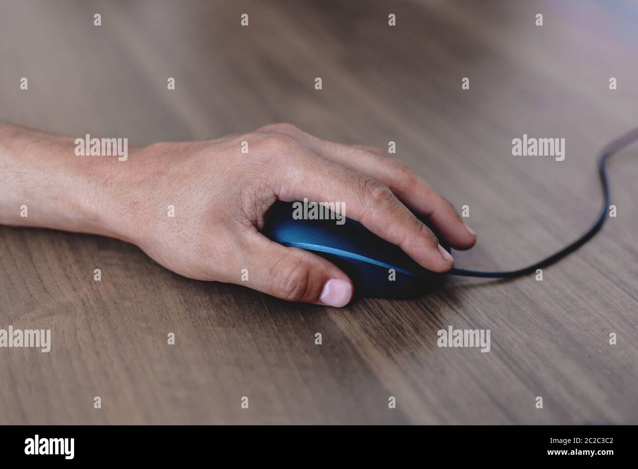 Ein Mann benutzt eine Computermaus auf einem Holztisch. Stockfoto