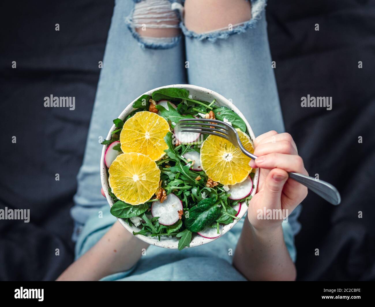 Frau in Jeans im Bett, mit veganer Salatschüssel Stockfoto