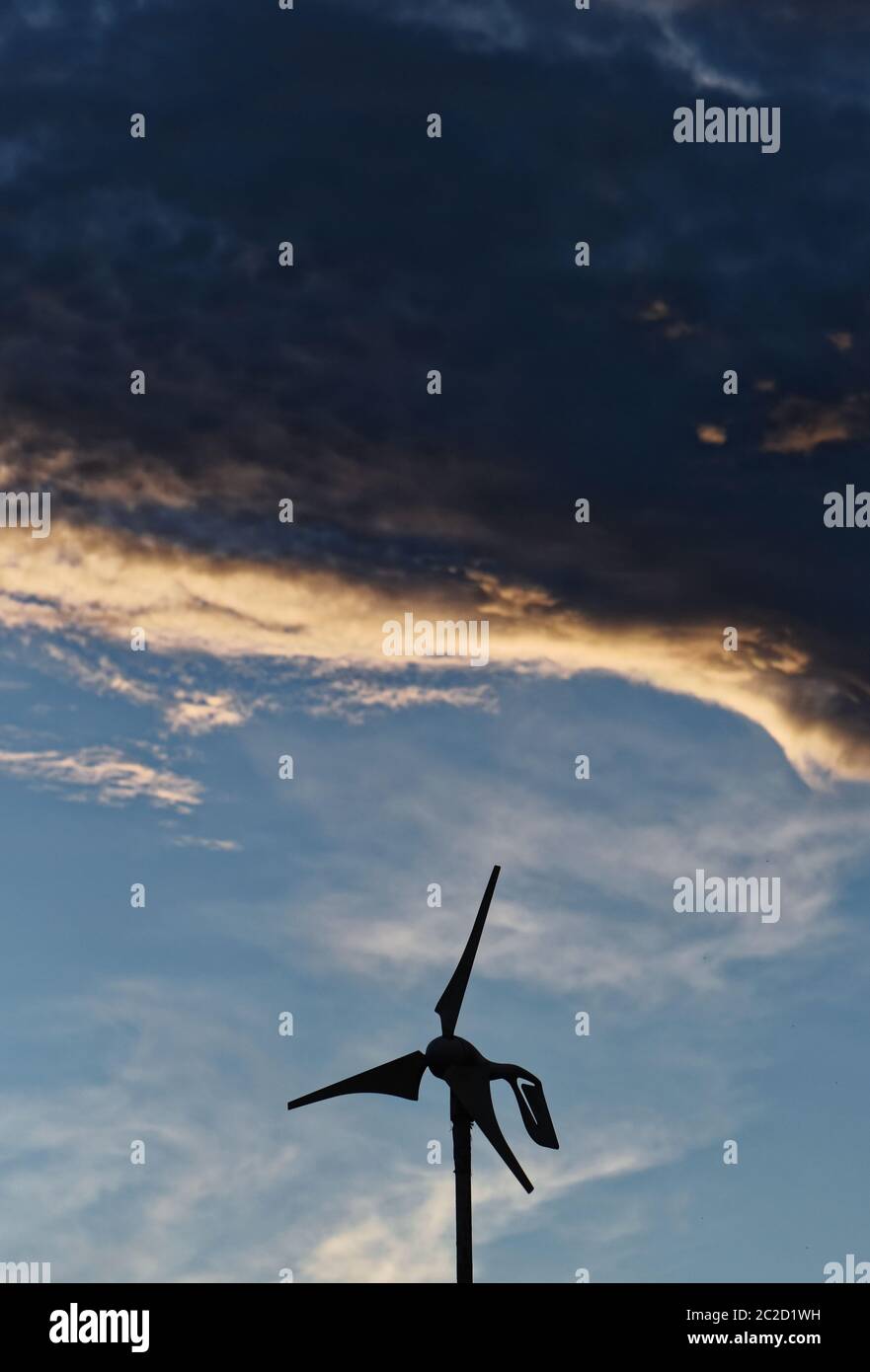 Der Rand der niedrigen grauen Wolken beleuchtet durch die Einstellung über einer Windkraftanlage. Stockfoto