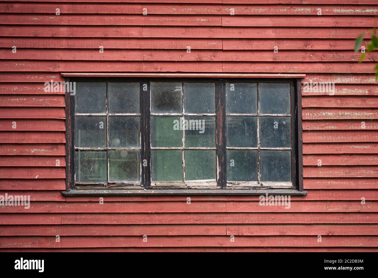 Alte verwitterte rustikale und schmutzige Fenster in einem alten rot gestrichenen Holzgebäude. Nahaufnahme von außen. Stockfoto