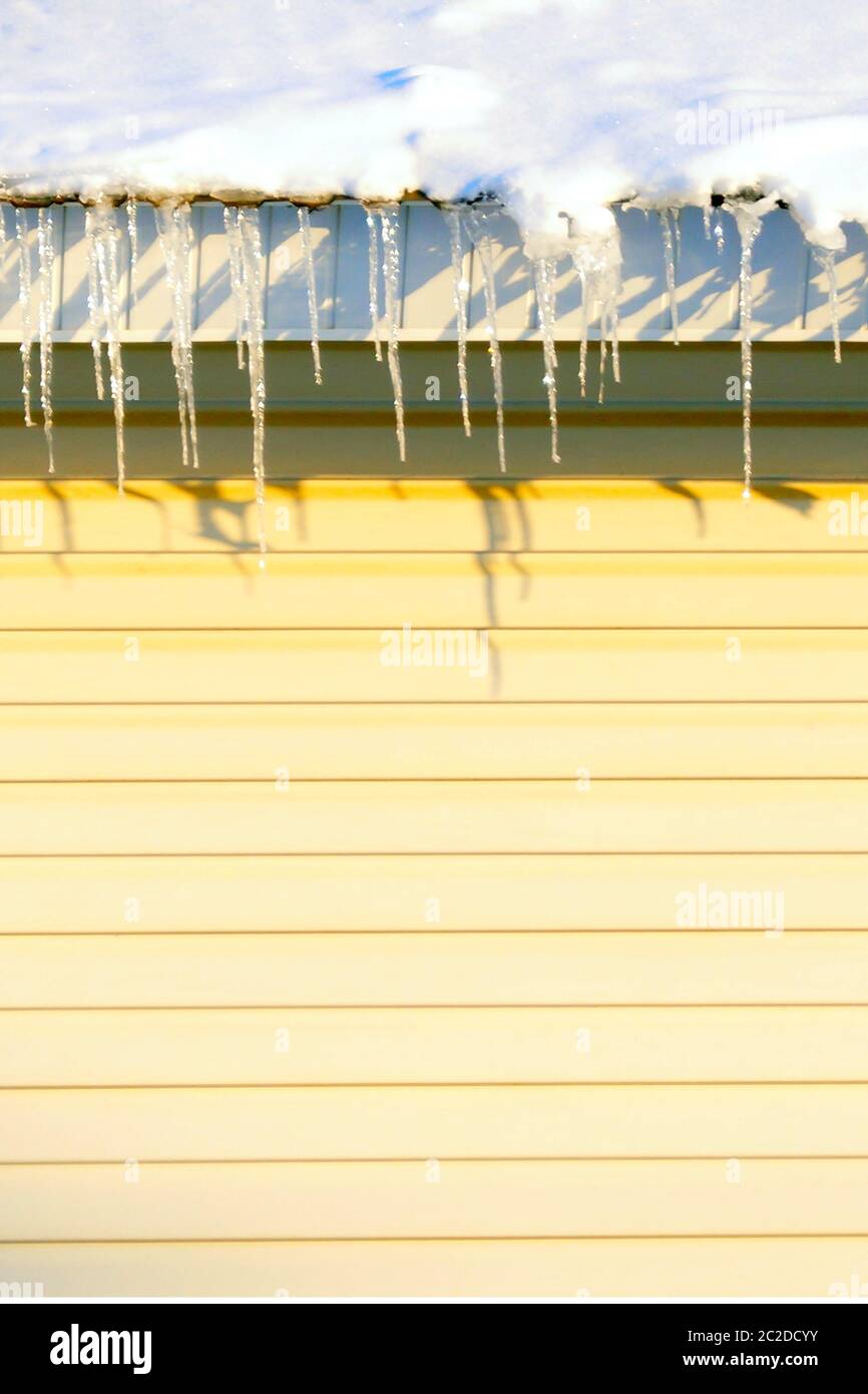 Viele große und scharfe Eiszapfen hängen auf dem Dach des Hauses. Stockfoto