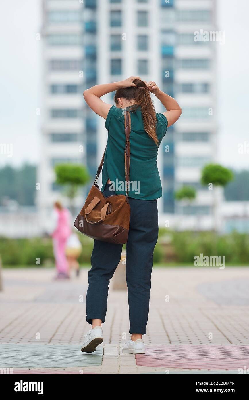 Eine junge Frau steht mit dem Rücken und bindet ihr Haar an den Schwanz in der Mitte der Stadt. Ein Mädchen in stilvollen Freizeitkleidung ist die soziale Distanz zu halten Stockfoto