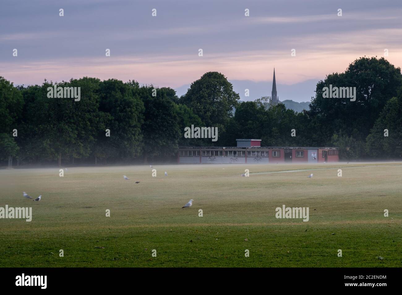 Nebel steigt aus dem Spielfeld des Eastville Park bei Sonnenaufgang in North Bristol, mit Stapleton Kirche Kirchturm in der Ferne. Stockfoto