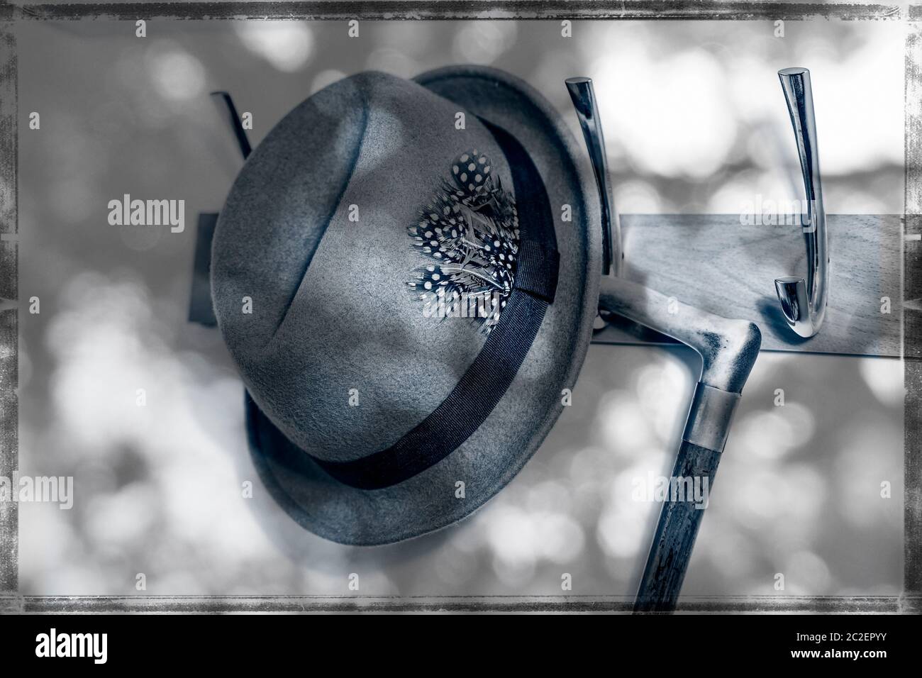 Arty, monochrome Nahaufnahme der 40er Jahre, Vintage Trilby Hut der 1950er Jahre, Fedora Hut und altmodischer Gehstock, der in gedappltem Sonnenlicht auf der Garderobe aufgehängt wird. Stockfoto
