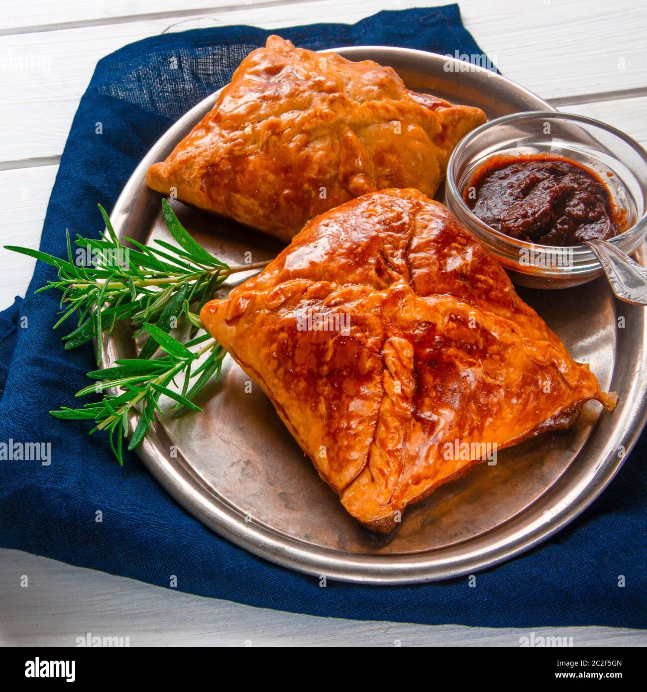 Hausgemachte Backwaren mit Fleisch und würziger Sauce mit Rosmarin auf einem Metalltablett auf weißem Holztisch serviert Stockfoto