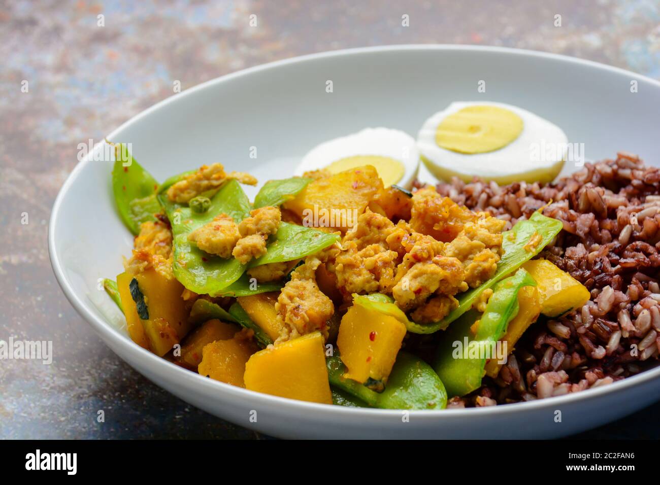 Pfannengerichte Zuckerschoten mit Kürbis und Huhn, serviert mit braunem Reis und gekochtem Ei Stockfoto