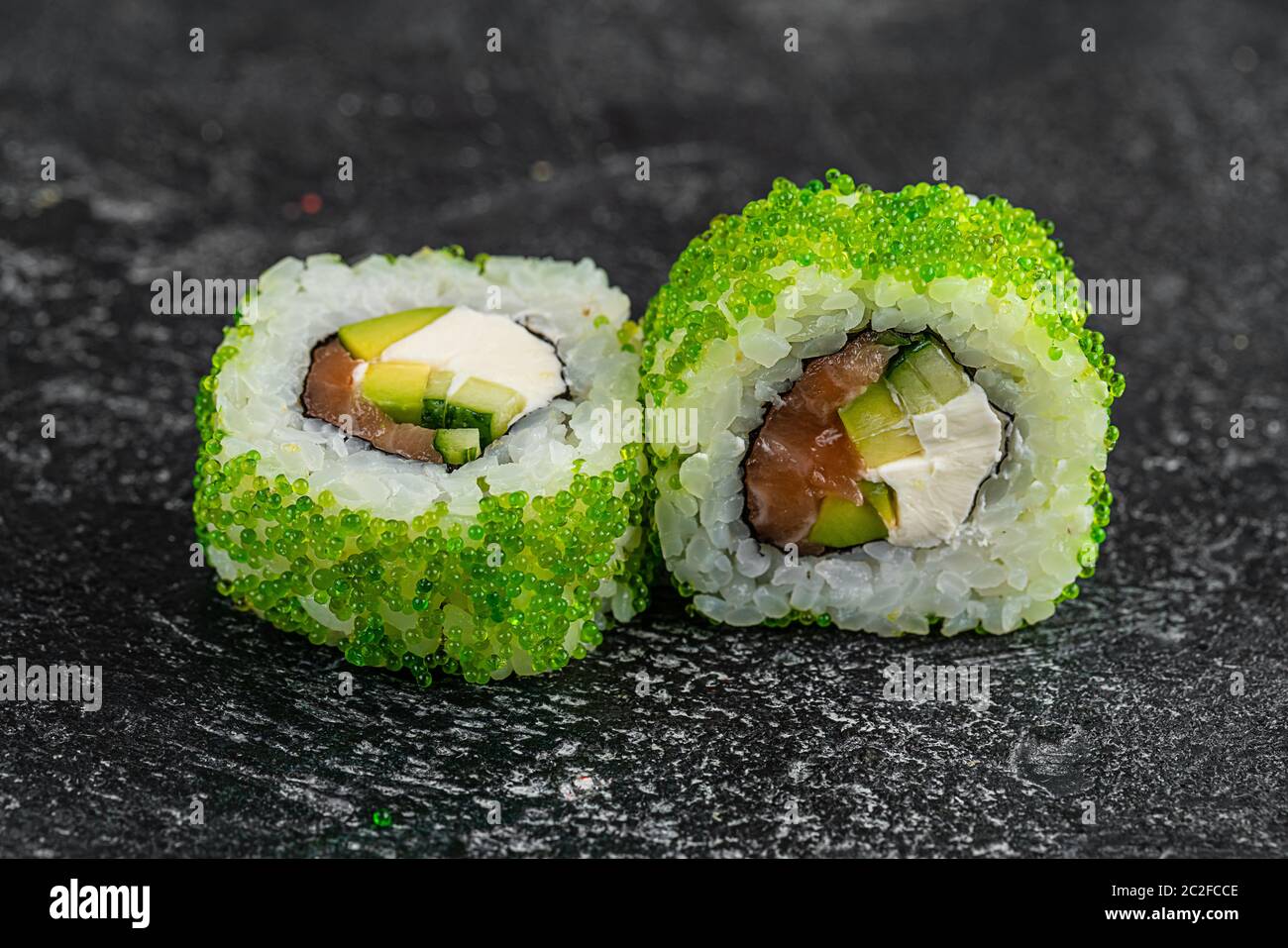 Sushi-Brötchen mit Tobiko Green Caviar, Frischkäse und Fisch auf schwarzem Holztisch Hintergrund Stockfoto