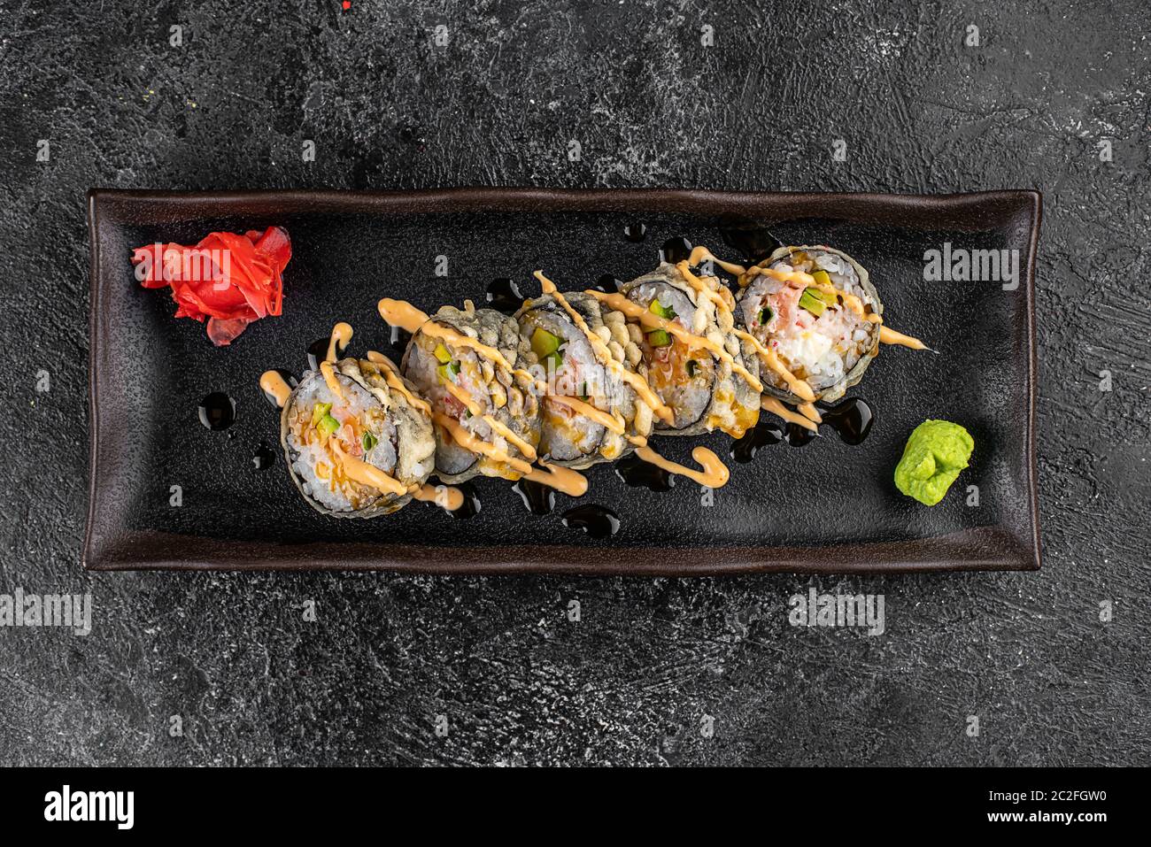 Gebackene Sushi-Brötchen mit Wasabi und Ingwer auf schwarzem Hintergrund. Japanische orientalische Küche Stockfoto