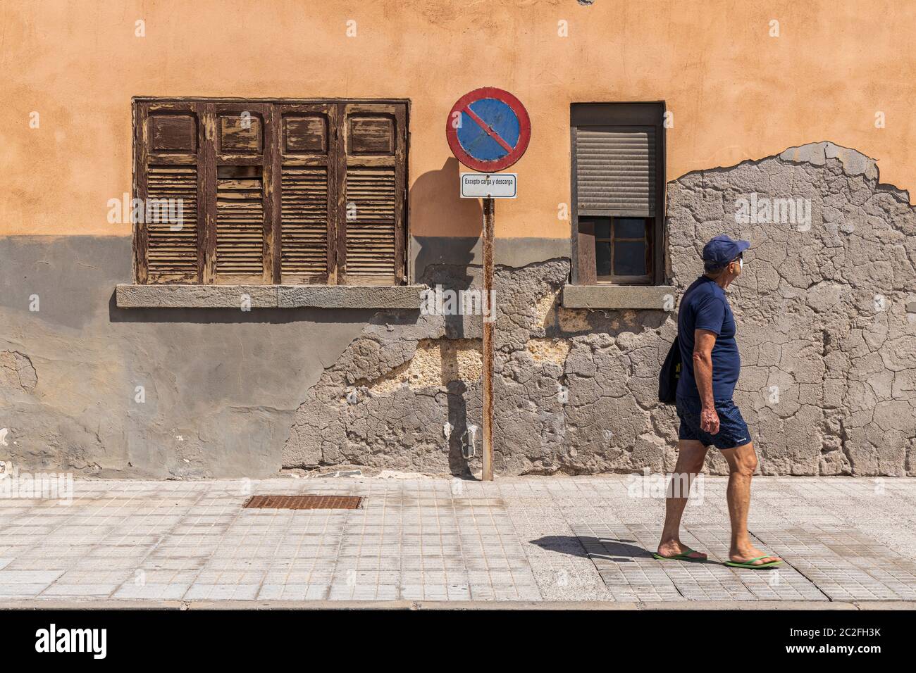 Mann in Shorts und T-Shirt mit Gesichtsmaske geht vorbei an alten notleidenden Fassade eines Gebäudes in El Medano, Teneriffa, Kanarische Inseln, Spanien Stockfoto