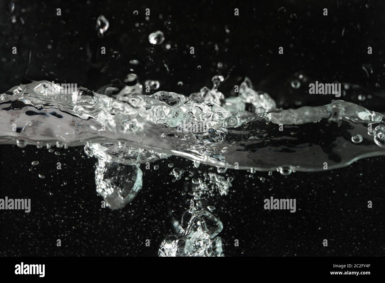 Wasser spritzt, wenn es in Aquarienbehälter gegossen wird, schwarzer Hintergrund Stockfoto
