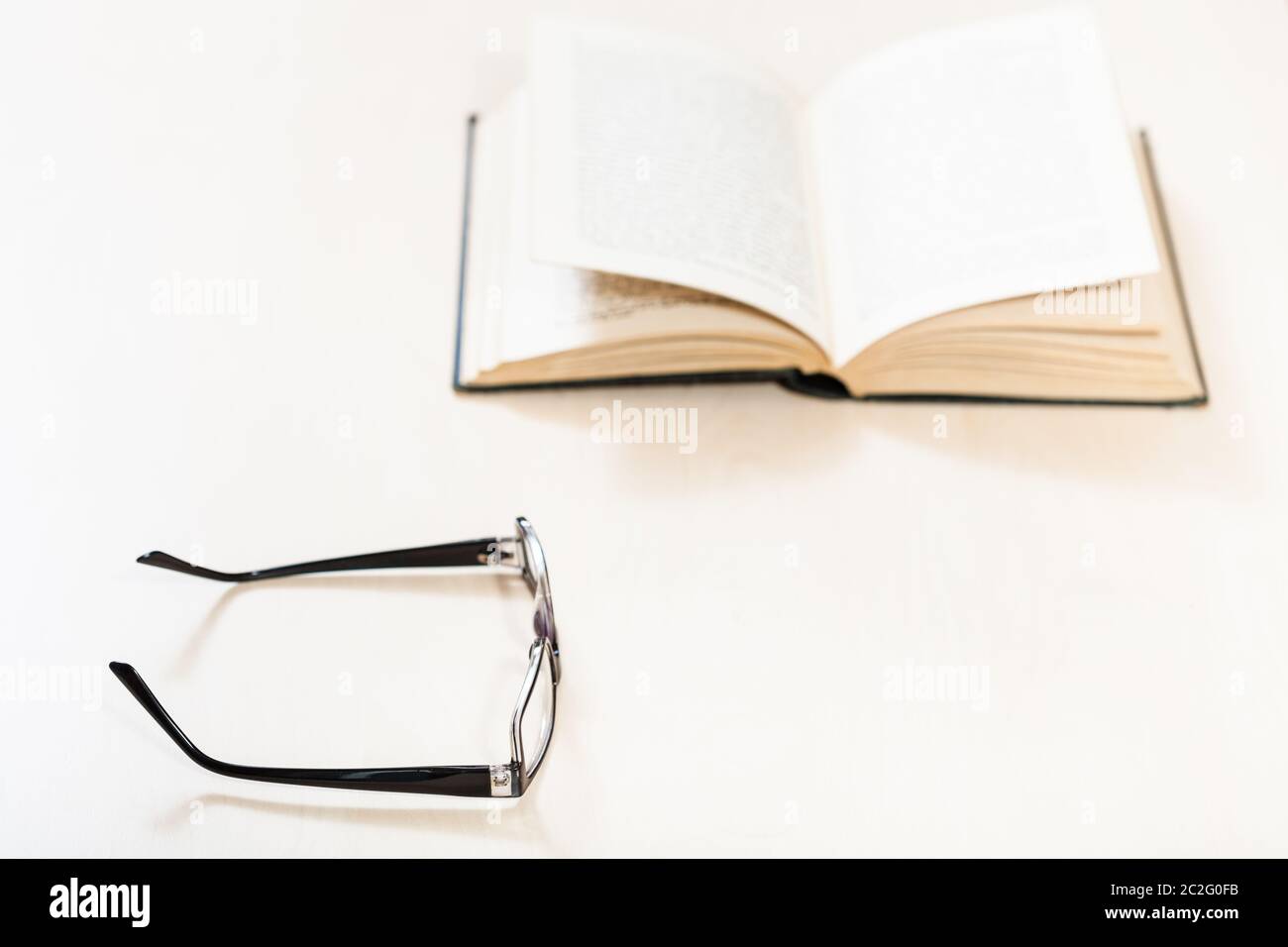 Lesen Buch mit Low Vision - Brillen und offenes Buch auf blass Tabelle (Schwerpunkt im Vordergrund) Stockfoto