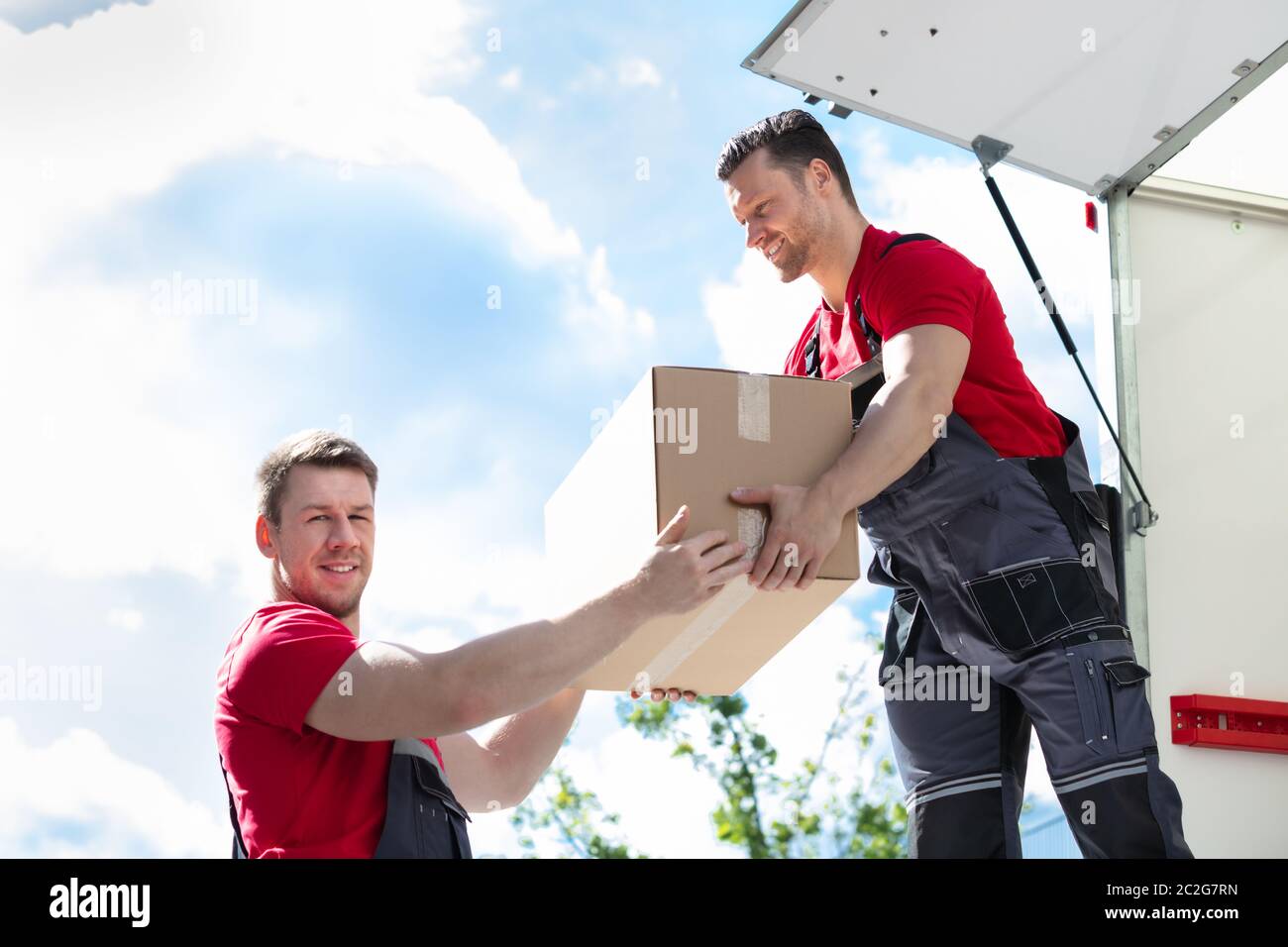 Männliche Movers Entladen und ein Karton zu seinem Assistenten in Moving Van Stockfoto