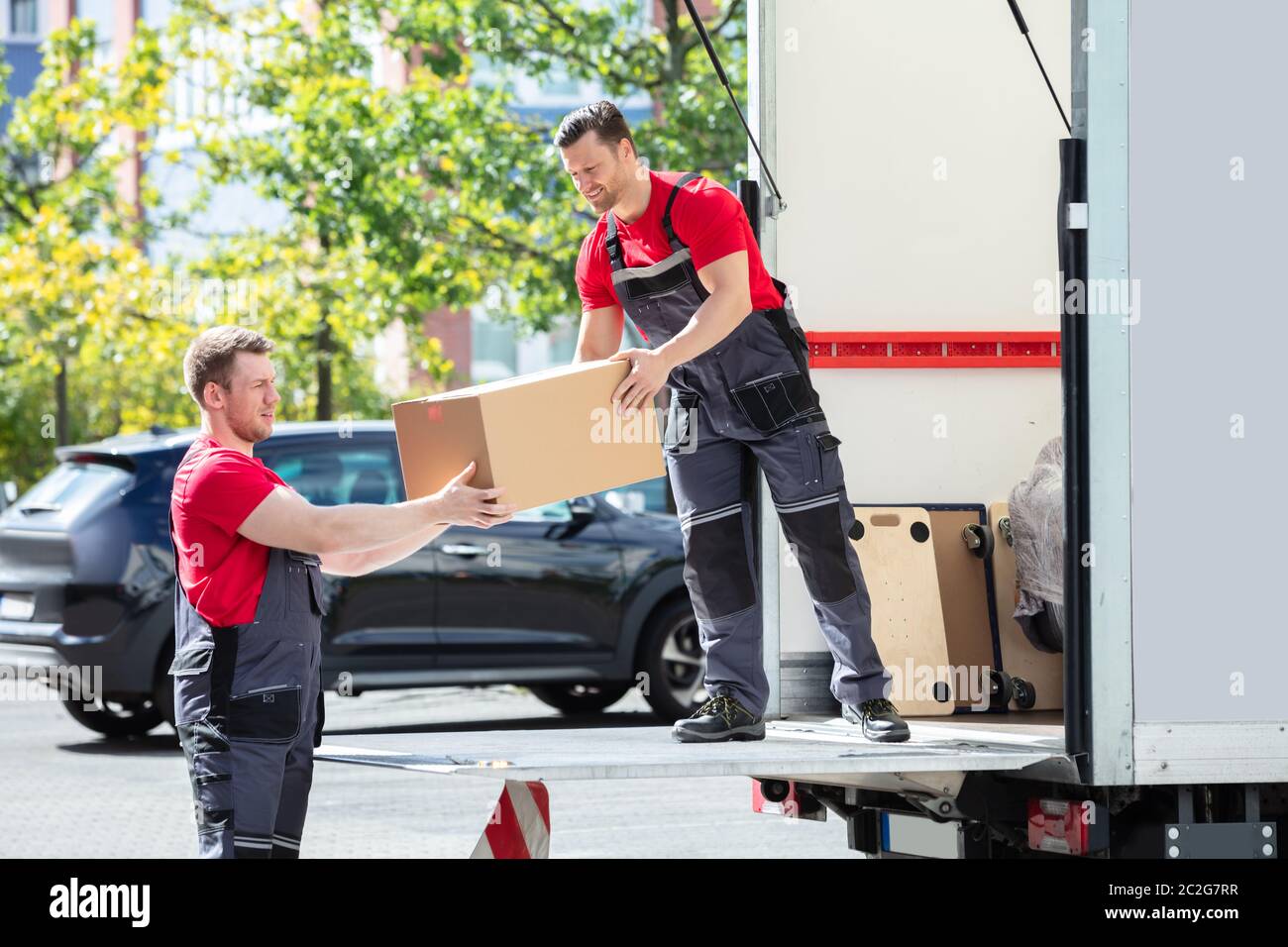 Männliche Movers Entladen und ein Karton zu seinem Assistenten in Moving Van Stockfoto