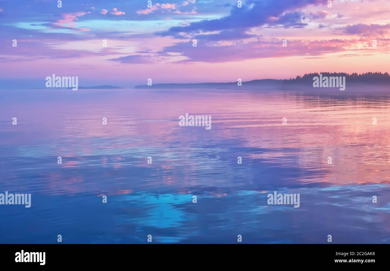 Neblige Seenlandschaft - ruhige Wasseroberfläche des Sees reflektiert lila Himmel mit rosa und blauen Wolken nach Sonnenuntergang. Weiße Nächte Saison in der Republik Kare Stockfoto