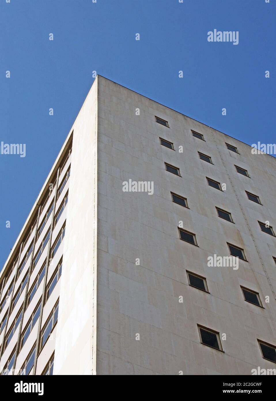 Perspektivische Eckansicht eines alten weißen Büroblocks aus Beton der 1960er Jahre gegen einen blauen Himmel Stockfoto