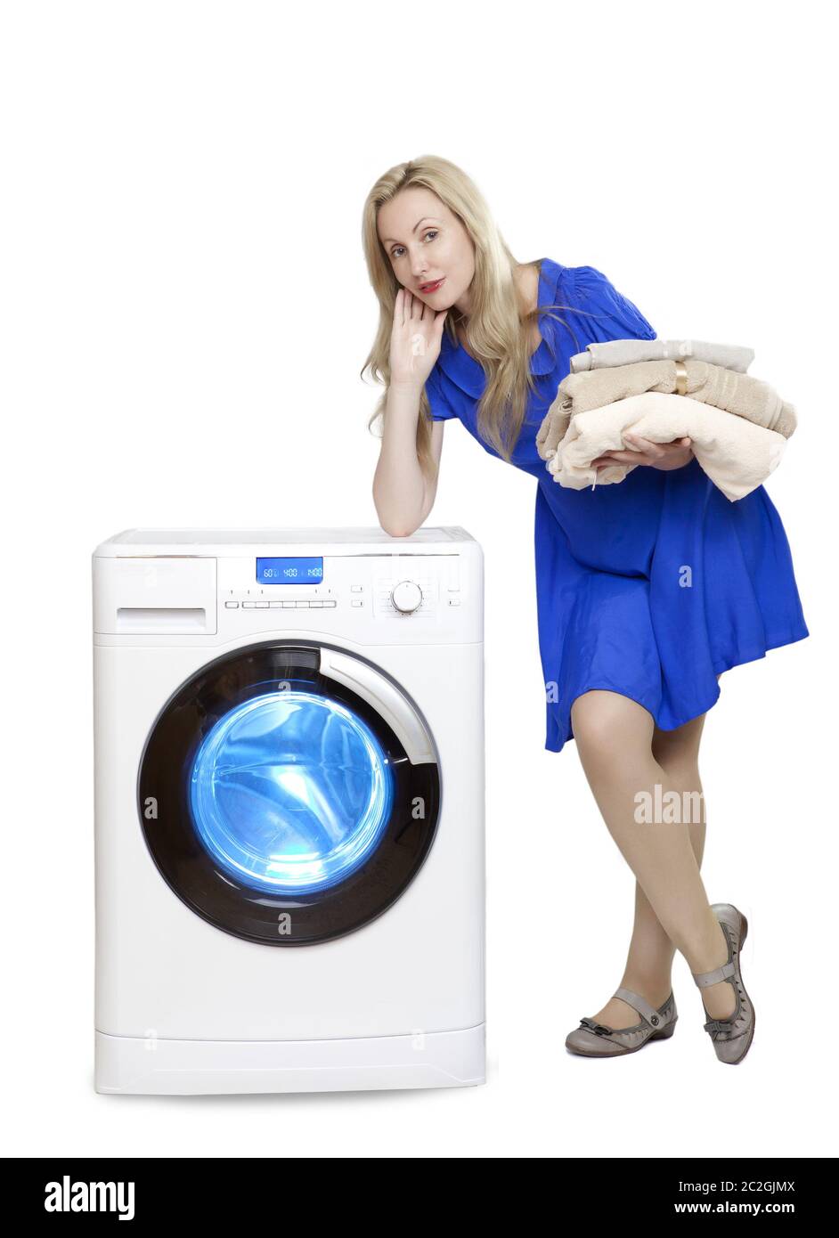 Schöne Frau in einem blauen Kleid weiter zu einer neuen Waschmaschine hält einen Stapel saubere Wäsche Stockfoto