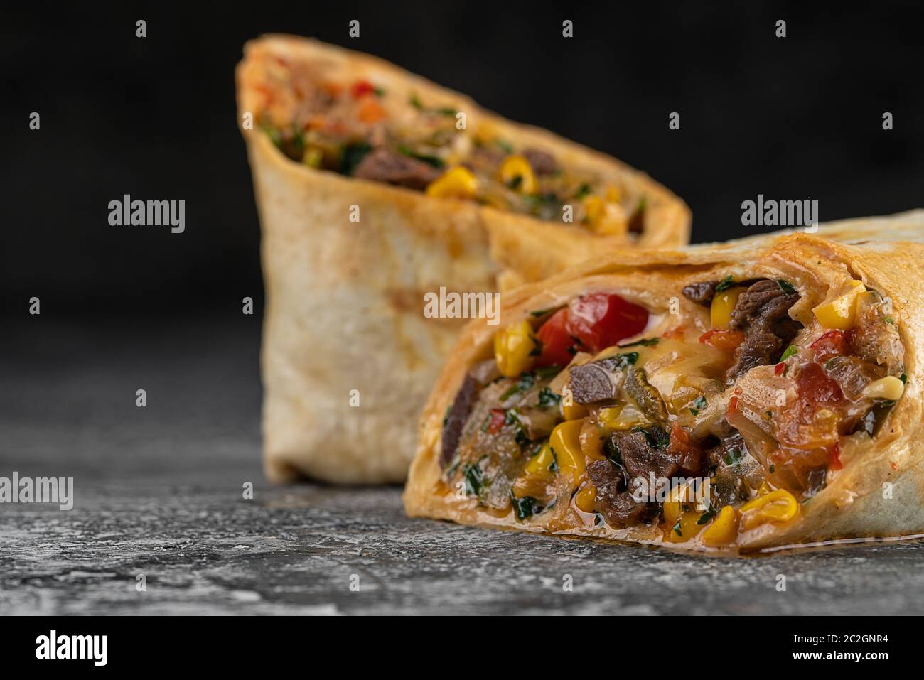 Burrito und Shawarma Wraps mit Rindfleisch und Schweinefleisch Gemüse auf Holztisch auf schwarzem Hintergrund Stockfoto