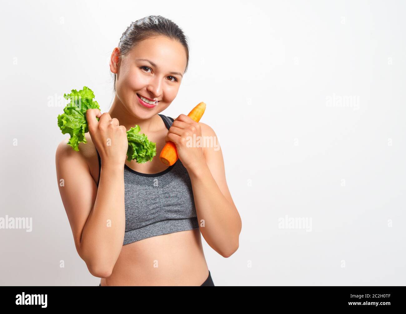 Schlanke junge Frau mit einer schönen Figur hält Gemüse in den Händen - Karotten und Salat Stockfoto