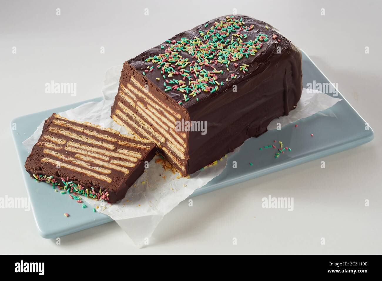 Close-up hohen Winkel von Schokolade Kuchen Kalter Hund mit Schichten von Butter Kekse im Inneren, bunte Topping und Vereisung, auf blau Keramik Tablett auf Wh serviert. Stockfoto