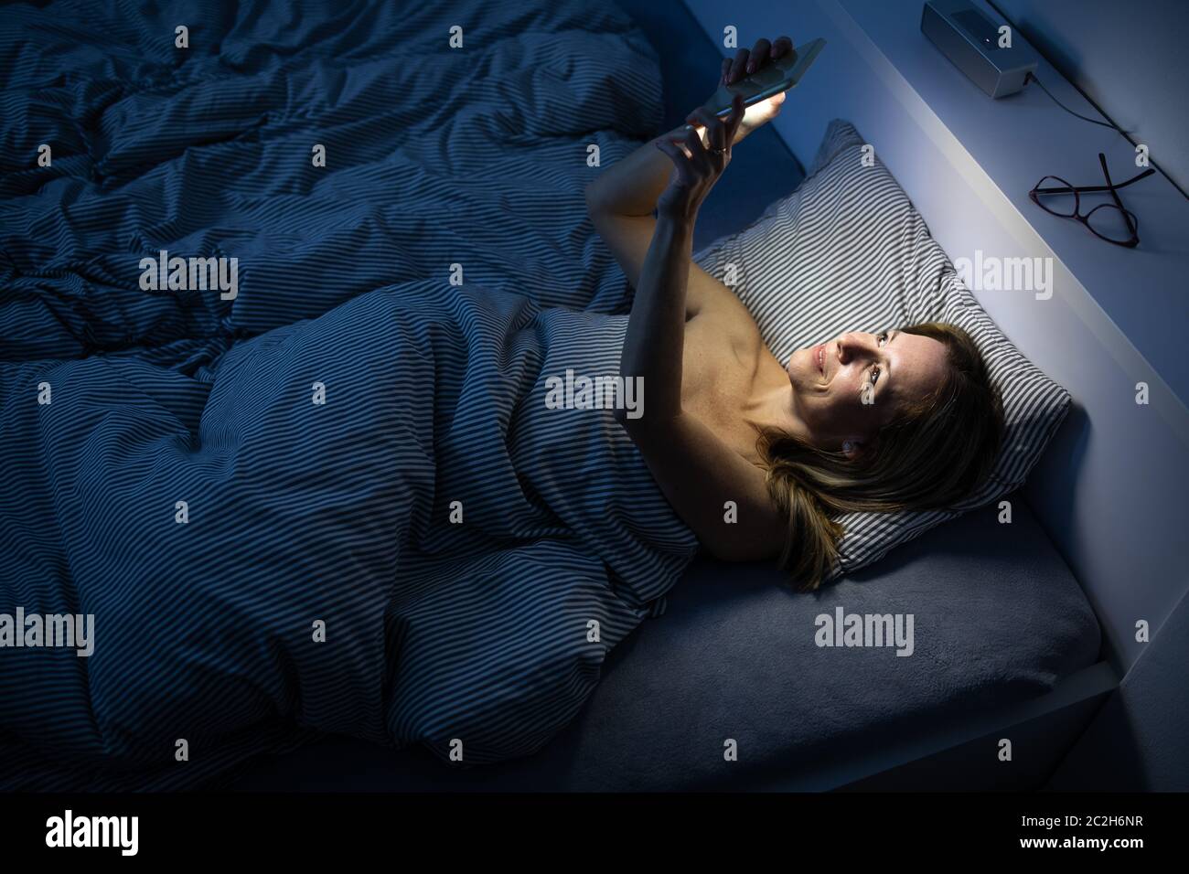 Hübsche Frau mittleren Alters mit Ihrem Handy in Bett zu Hause vor dem Schlaf Stockfoto