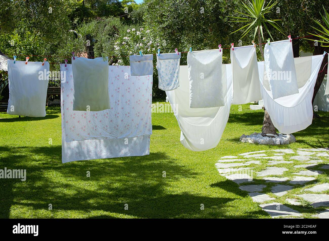 Wäsche der Bettwäsche und Kissen trocknen an einem sonnigen Tag in einem Garten mit grünem Gras einer Sommerhaus Villa. Stockfoto