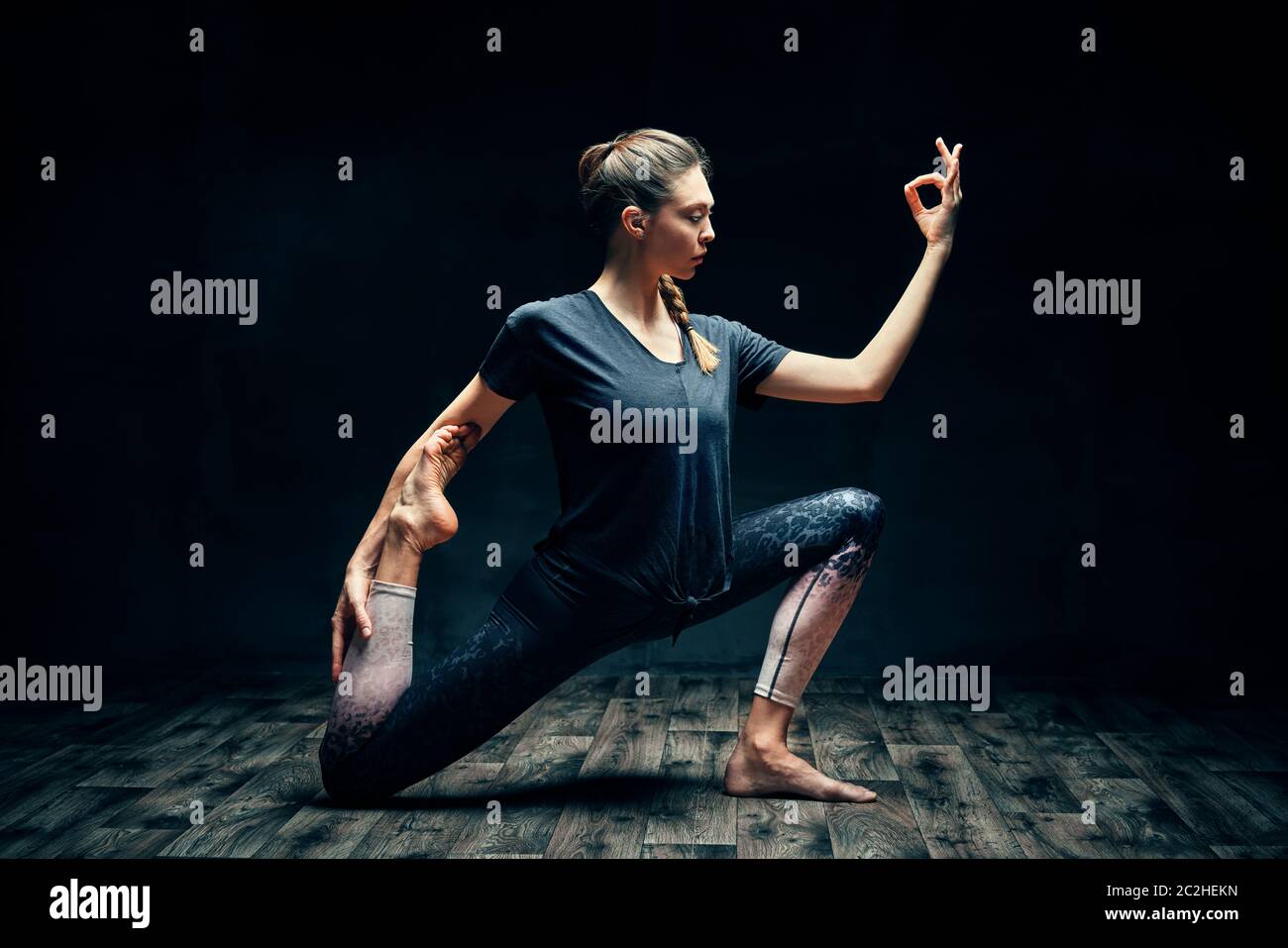 Junge schöne Frau, die Yoga Asana einbeinigen König Taube Pose in dunklen Raum Stockfoto