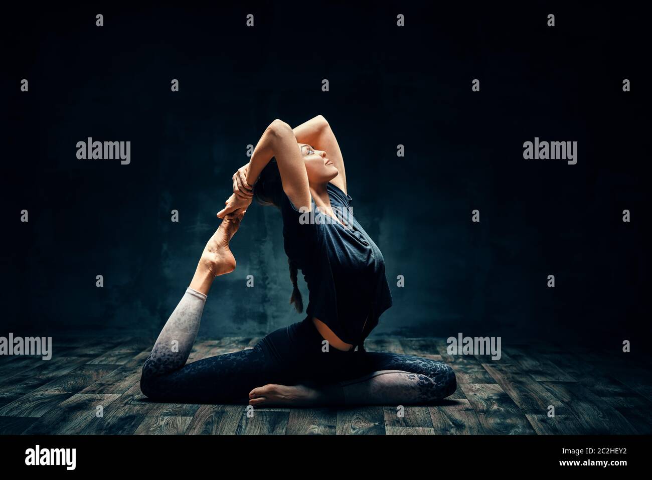 Junge Frau praktiziert Yoga dabei eine beinige Königstaube Pose in dunklen Raum Stockfoto