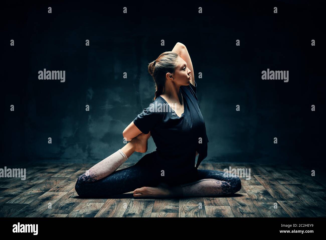 Junge Frau praktiziert Yoga dabei eine beinige Königstaube Pose in dunklen Raum Stockfoto