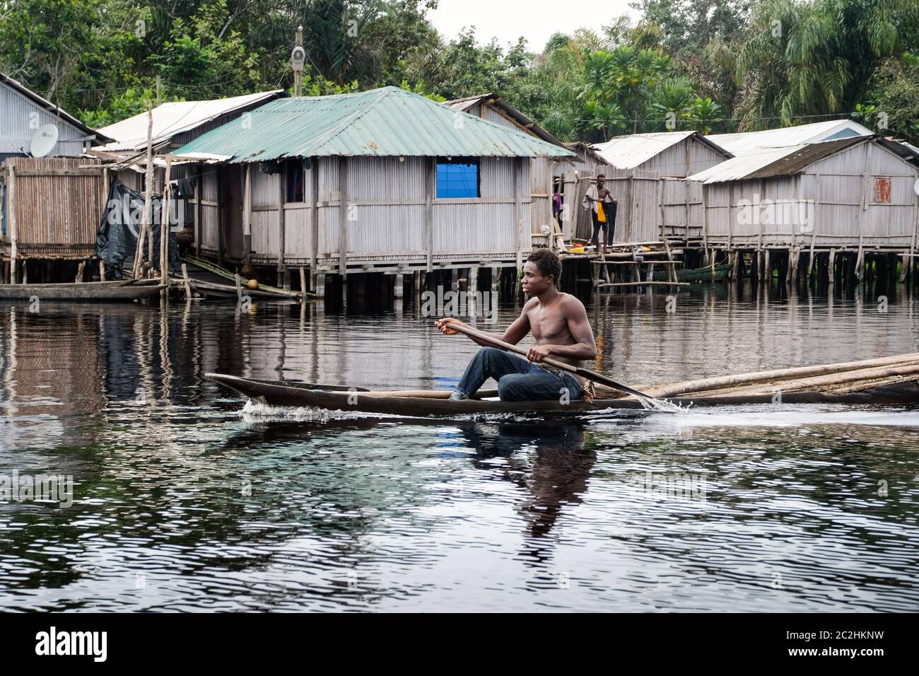 Mann in einem Ausgußboot vor den Hütten des Stelzendorfes Nzulezo im Amansura See, Ghana, Afrika Stockfoto